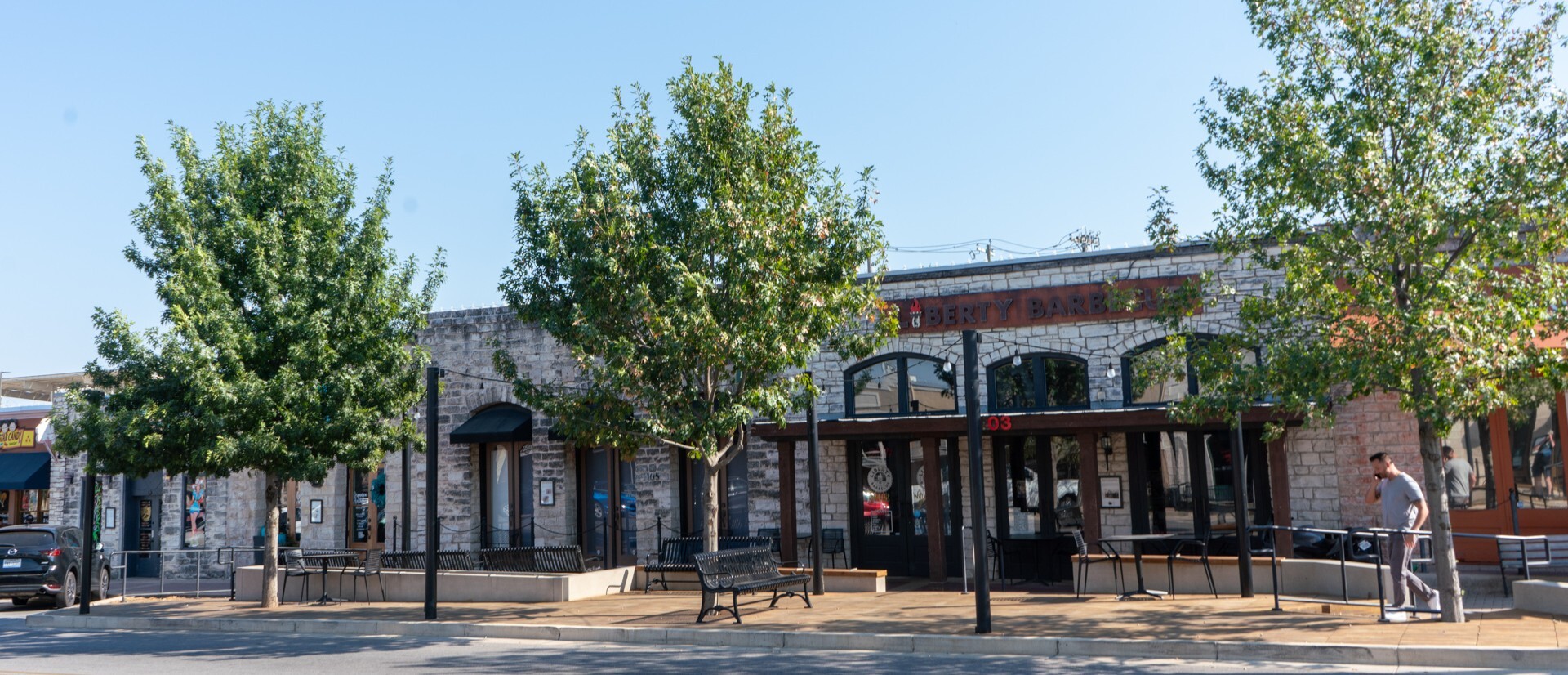 Row of three green urban trees on a sidewalk next to a street